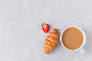 Cup of coffee and freshly baked croissants, strawberry on gray background.