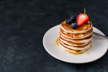 A stack of pancakes with berries honey on dark background