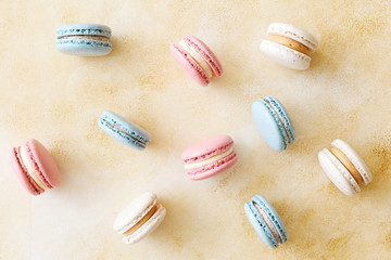 Minimalistic composition with bunch of french macaron sweets of different color and taste scattered over yellow grunged concrete texture background. Top view, close up, flat lay, copy space.