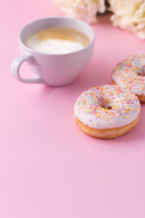 Mug of hot cappuccino with two donuts on a pink background.