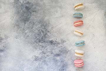 Minimalistic composition with bunch of french macaron sweets of different color and taste forming a frame over grunged concrete texture background. Top view, close up, flat lay, copy space.