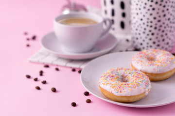 Mug of hot cappuccino with two donuts on a pink background.