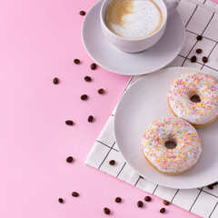 Mug of hot cappuccino with two donuts on a pink background
