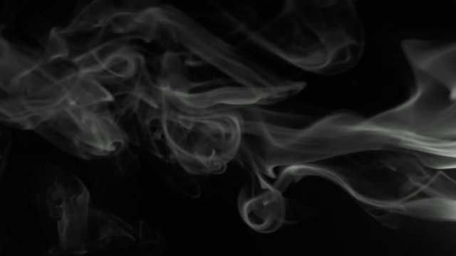 Vertical video:  Trickle gray smoke slowly rising graceful twists upward. Black and white cigar smoke blowing from the right side. Closeup, isolated on black background.