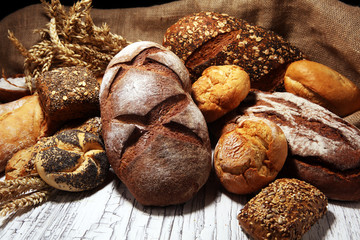 Assortment of baked bread and bread rolls on rustic white bakery table background