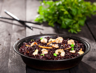 Cooked black rice with shrimps and vegetables in a dish on the wood background.
