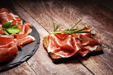 Italian prosciutto crudo or jamon with rosemary. Raw ham on wooden board