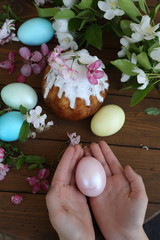 Easter egg in the hands of a child and a cake in sugar icing on a wooden table