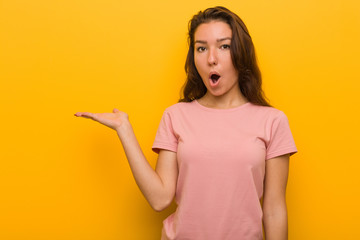 Young european woman isolated over yellow background impressed holding copy space on palm.
