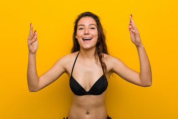 Young european woman wearing bikini receiving a pleasant surprise, excited and raising hands.