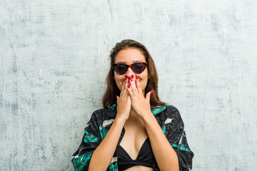 Young european woman wearing bikini laughing about something, covering mouth with hands.