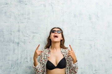 Fototapeta premium Young european woman wearing bikini indicates with both fore fingers up showing a blank space.