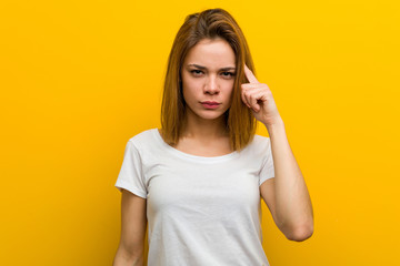 Young natural caucasian woman pointing her temple with finger, thinking, focused on a task.