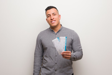 Young latin man holding an air tickets cheerful with a big smile
