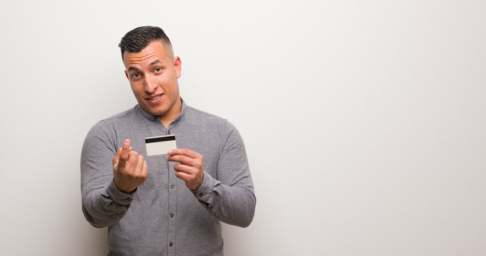 Young latin man holding a credit card inviting to come