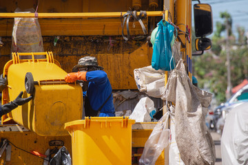 Worker of urban municipal recycling garbage collector truck loading waste and trash bin in morning.