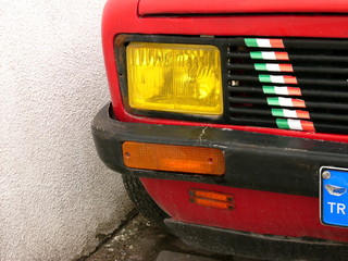 Gelber Scheinwerfer einer Stufenheck Limousine in Rot der Siebzigerjahre aus Italien auf dem...