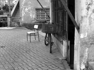 Plakat Altes Fahrrad und bequemer Stuhl auf grauem Straßenpflaster vor einem Geschäft in Adapazari in der Provinz Sakarya in der Türkei, fotografiert in neorealistischem Schwarzweiß