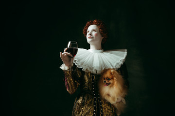 Dreaming. Medieval redhead young woman in golden vintage clothing as a duchess holding puppy and...