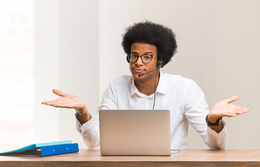 Young telemarketer black man doubting and shrugging shoulders