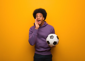 Young african american sport man holding a soccer ball shouting something happy to the front