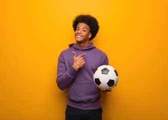 Young african american sport man holding a soccer ball inviting to come