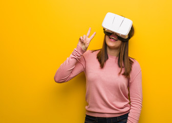 Young cute woman wearing a virtual reality googles fun and happy doing a gesture of victory