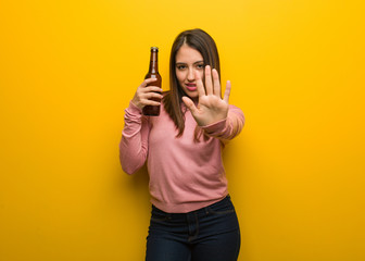 Young cute woman holding a beer putting hand in front