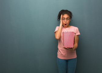 Young black woman surprised and shocked. She is holding a popcorns bucket.