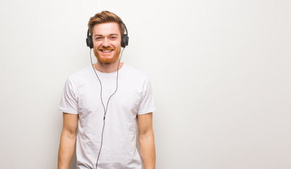Fototapeta premium Young redhead man cheerful with a big smile. Listening to music with headphones.