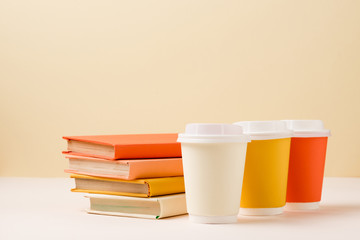 stack of books and colorful disposable cups on white surface isolated on beige