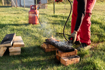 A man burns wooden planks with propane using old-time Japanese technology, creating facing material for building a house