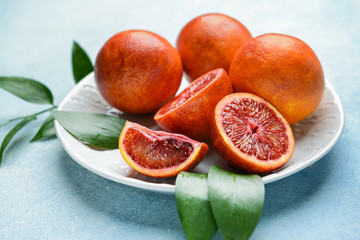 Plate with fresh blood oranges on color background