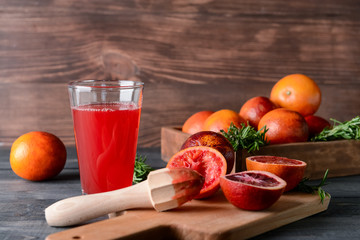Glass of fresh blood orange juice with fruit and juicer on wooden table