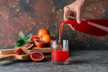 Woman pouring fresh blood orange juice from jug into glass on table