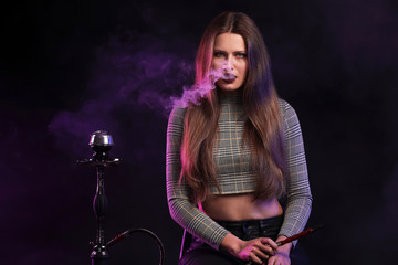 Fototapeta na wymiar Young woman smoking hookah on dark background