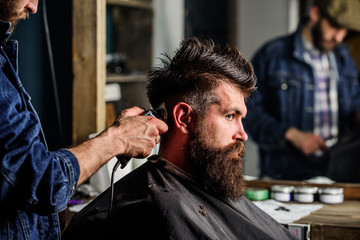 Barber styling hair of brutal bearded client with clipper. Barber with hair clipper works on...
