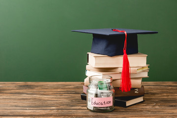 books, academic cap and piggy bank on wooden surface isolated on green
