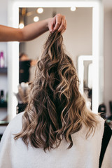Naklejka premium Beautiful brunette woman with long hair at the beauty salon getting a hair blowing. Hair salon styling concept.