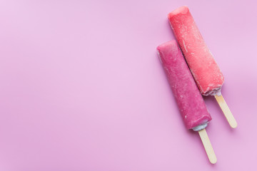 Bright fruit ice cream on a stick on a pink background. Frozen fruit ice. Summer mood. Cooling dessert in hot weather. Favorite delicacy for children. Homemade raspberry, strawberry, watermelon ice