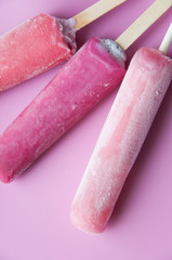 Bright fruit ice cream on a stick on a pink background. Frozen fruit ice. Summer mood. Cooling dessert in hot weather. Favorite delicacy for children. Homemade raspberry, strawberry, watermelon ice