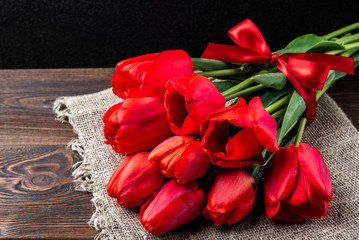 Naklejka na ściany i meble Red tulips with red ribbon on dark wooden background.