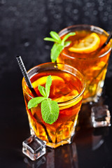 Two glasses with cold traditional iced tea with lemon, mint leaves and ice cubes.