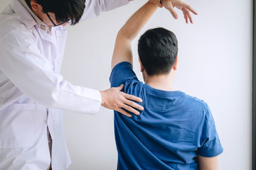 Doctor physiotherapist assisting a male patient while giving exercising treatment massaging the shoulder of patient in a physio room, rehabilitation physiotherapy concept
