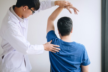 Doctor physiotherapist assisting a male patient while giving exercising treatment massaging the shoulder of patient in a physio room, rehabilitation physiotherapy concept - obrazy, fototapety, plakaty