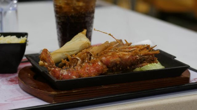 Large fried prawn on hot pan with green, additional meal at affordable restaurant. Closeup shot of dark iron plate on wooden pad, vapour rise up from frizzling food