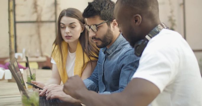 Ambitious multirace team working on startup project using laptop in outdoors cafe