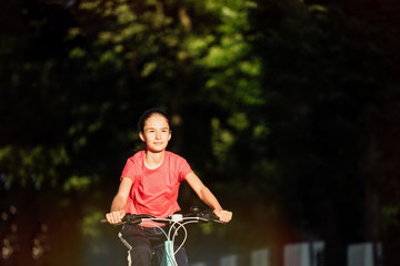 Obraz premium Girl Kid Riding Bike in Summer in City at Beautiful Sunset 