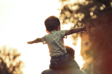 Happy family: Young father with his little child sitting on father's shoulders in Summer in City at...