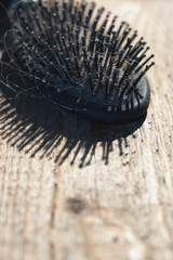 Black hairbrush with blonde hair on wooden floor.